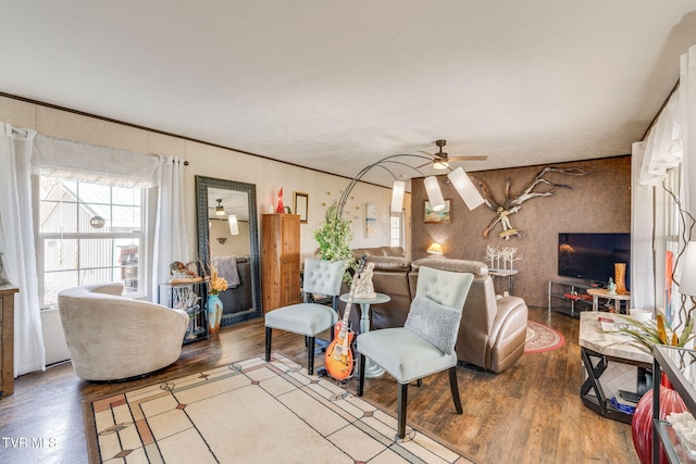 living area featuring wood finished floors, a ceiling fan, and crown molding