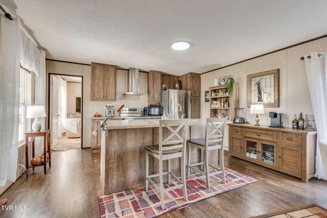 kitchen with dark wood-style flooring, stainless steel appliances, light countertops, brown cabinetry, and wall chimney range hood