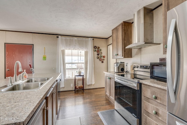 kitchen with appliances with stainless steel finishes, light countertops, a textured ceiling, wall chimney range hood, and a sink