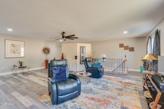 living area with recessed lighting, wood finished floors, a ceiling fan, an upstairs landing, and baseboards