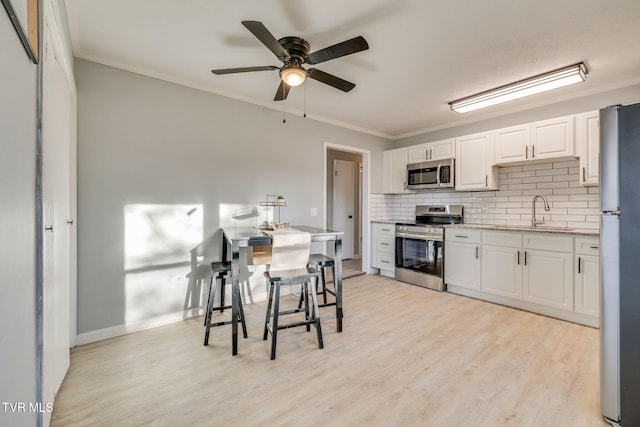 kitchen featuring a sink, white cabinetry, ornamental molding, appliances with stainless steel finishes, and backsplash