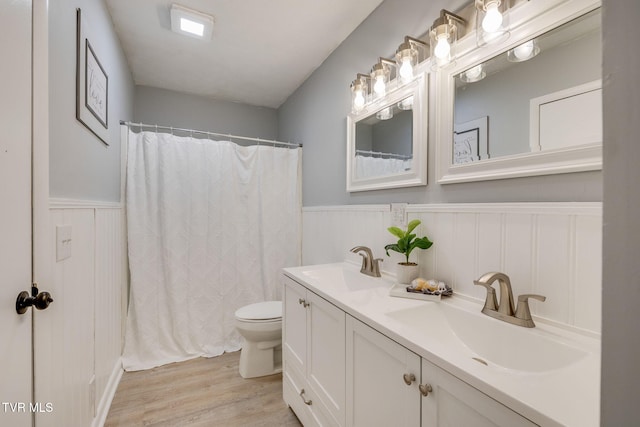 full bath featuring wainscoting, a sink, toilet, and wood finished floors