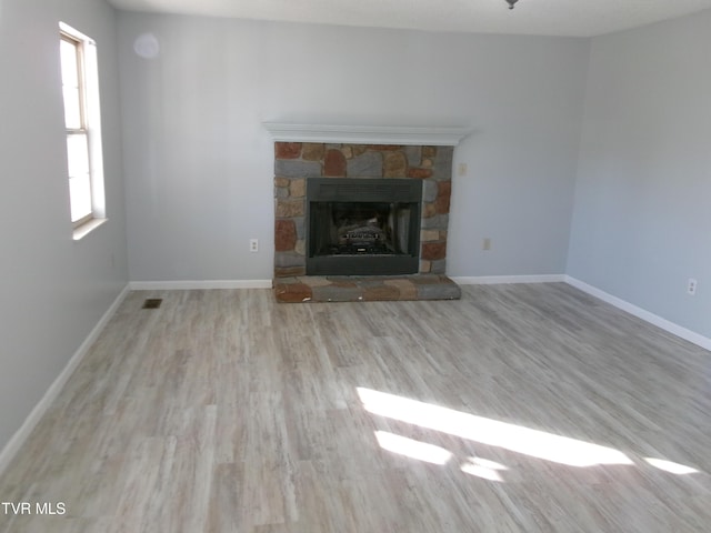 unfurnished living room featuring light wood finished floors, baseboards, and a stone fireplace