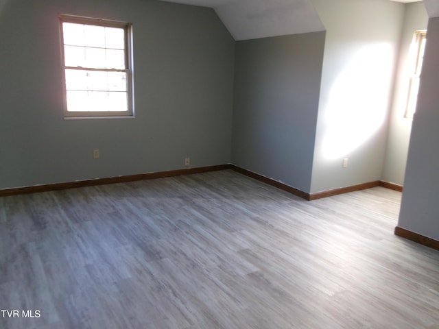 additional living space with light wood-style floors, vaulted ceiling, and baseboards