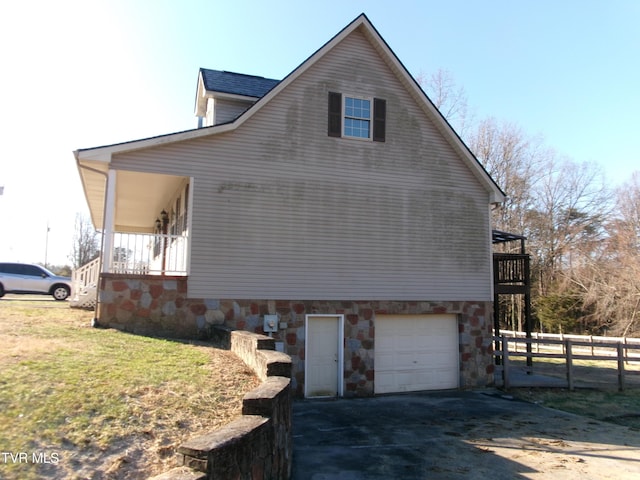 view of side of property with a garage, driveway, a balcony, fence, and a yard