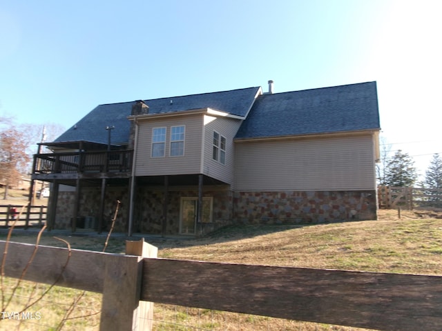 rear view of house with stone siding, a yard, a shingled roof, and fence