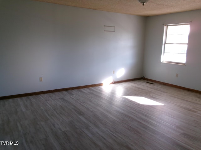 unfurnished room with visible vents, a textured ceiling, baseboards, and wood finished floors