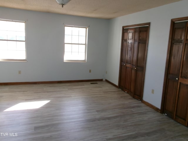 unfurnished bedroom featuring a textured ceiling, light wood-style flooring, and baseboards