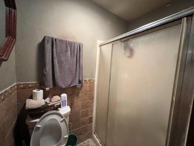 bathroom featuring toilet, a stall shower, tile walls, and wainscoting