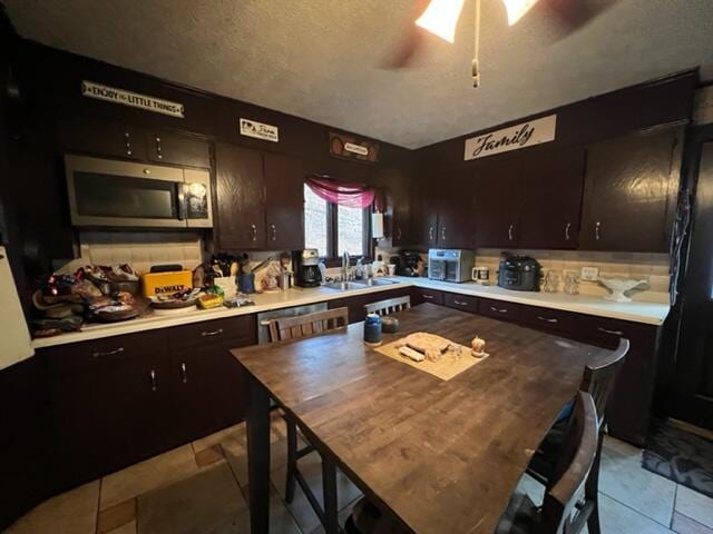 kitchen with light countertops, stainless steel microwave, a sink, and dark brown cabinets