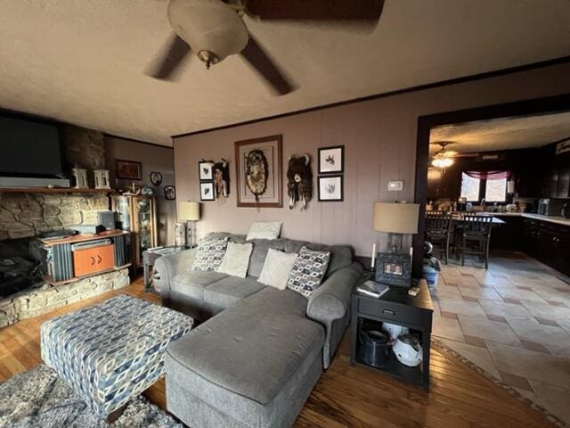 living area featuring a ceiling fan, a stone fireplace, and wood finished floors