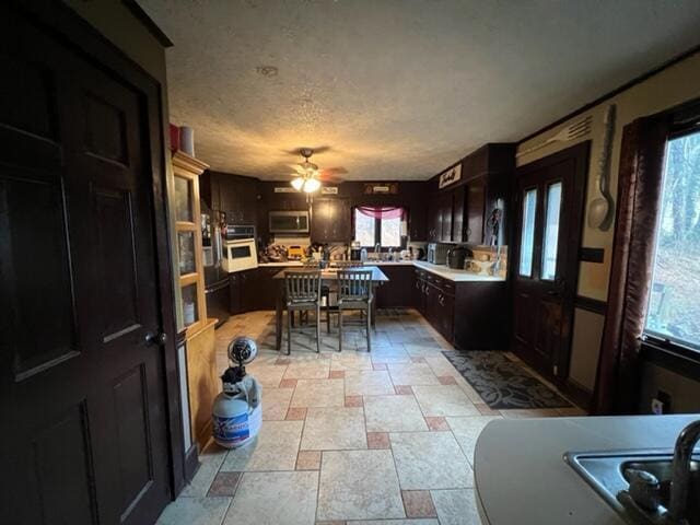 kitchen with white oven, light countertops, stainless steel microwave, ceiling fan, and a textured ceiling