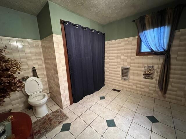 bathroom featuring a textured ceiling, toilet, tile patterned flooring, and tile walls