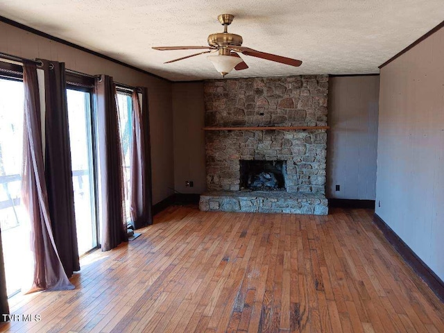 unfurnished living room with a ceiling fan, wood-type flooring, ornamental molding, a textured ceiling, and a stone fireplace