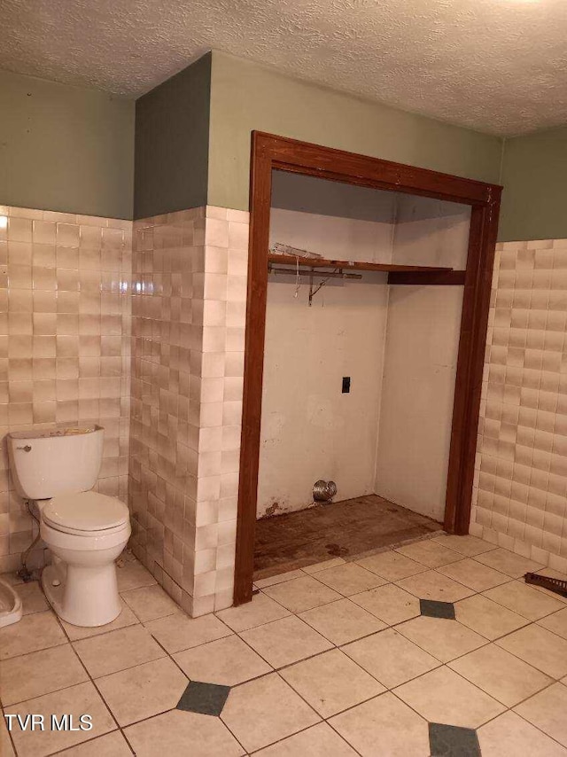 bathroom with tile patterned floors, tile walls, toilet, and a textured ceiling