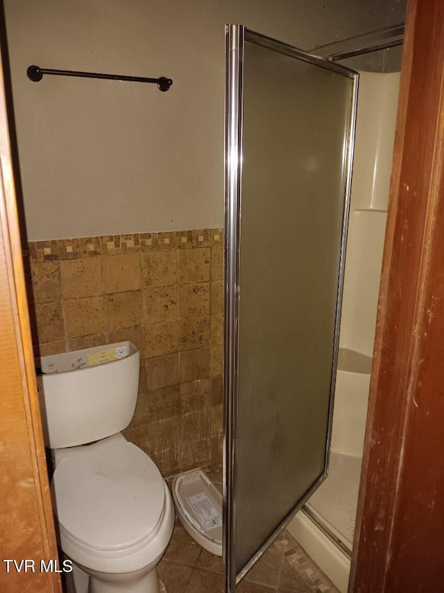 full bathroom featuring a stall shower, wainscoting, toilet, tile patterned floors, and tile walls