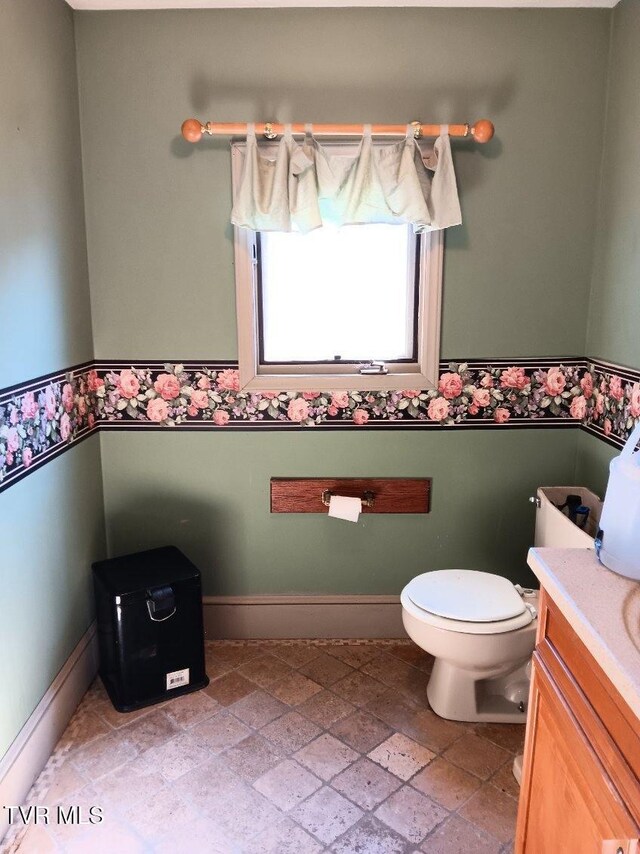 half bathroom featuring toilet, stone finish flooring, baseboards, and vanity