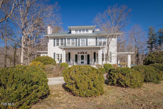 back of house with a chimney, covered porch, a lawn, and a balcony