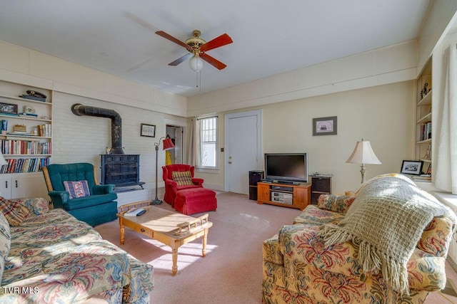 living room with ceiling fan, built in shelves, a wood stove, and light colored carpet