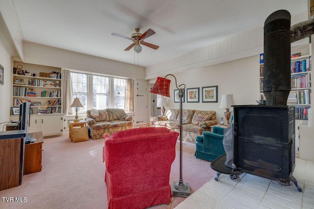 living room featuring a ceiling fan, a wood stove, and light colored carpet