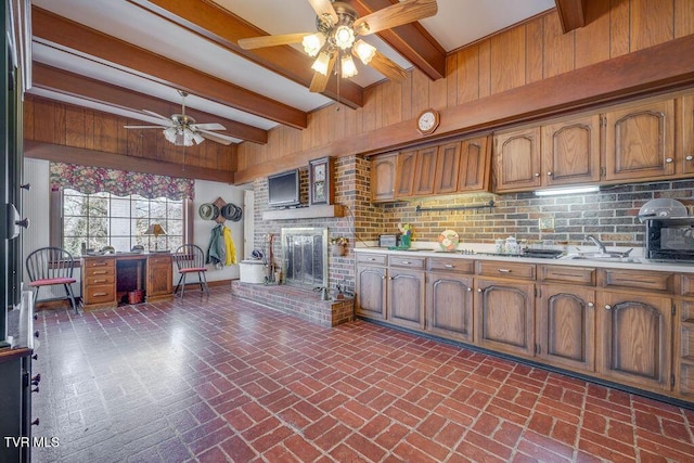 kitchen with brick floor, beam ceiling, brown cabinets, a fireplace, and light countertops