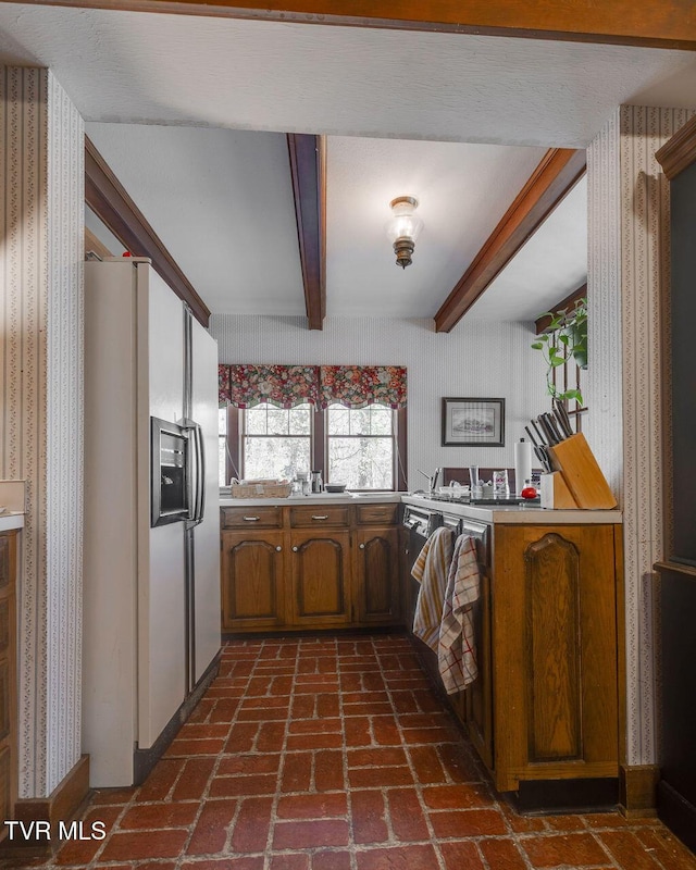 kitchen featuring brick floor, white refrigerator with ice dispenser, light countertops, beam ceiling, and wallpapered walls