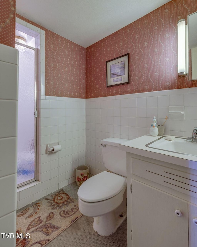 bathroom with tile walls, toilet, wainscoting, vanity, and wallpapered walls