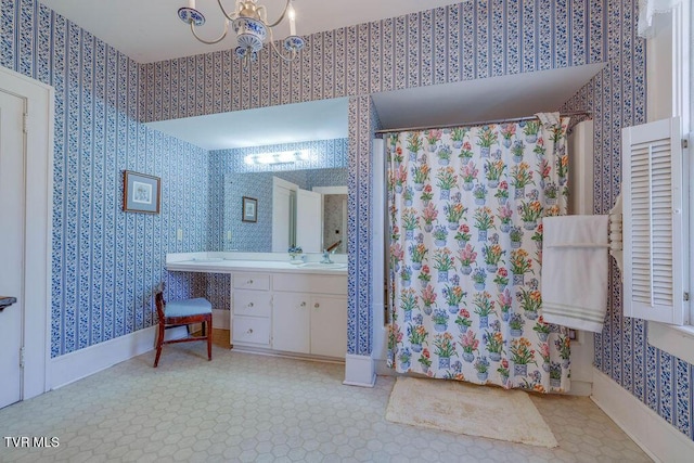 full bath with a chandelier, vanity, baseboards, and wallpapered walls