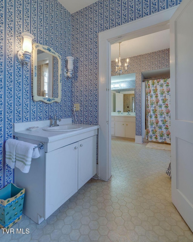 bathroom featuring two vanities, a sink, an inviting chandelier, and wallpapered walls