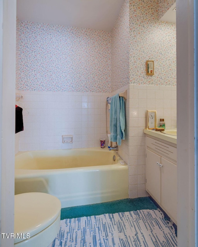 bathroom featuring wallpapered walls, wainscoting, toilet, vanity, and tile walls