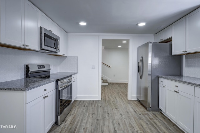 kitchen with light wood finished floors, tasteful backsplash, baseboards, stainless steel appliances, and white cabinetry