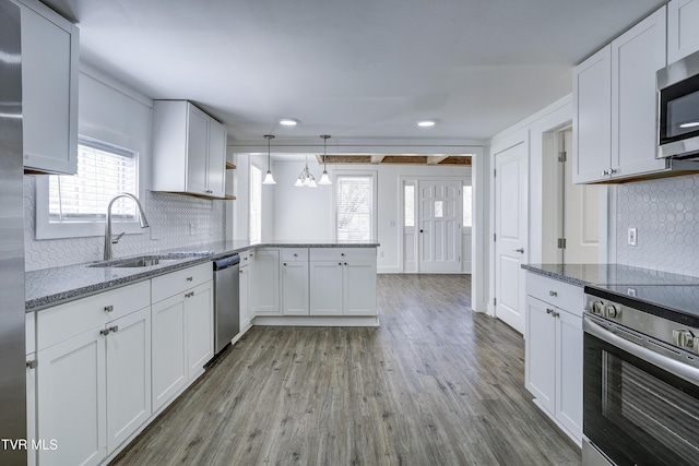 kitchen with a peninsula, stainless steel appliances, a sink, white cabinets, and hanging light fixtures