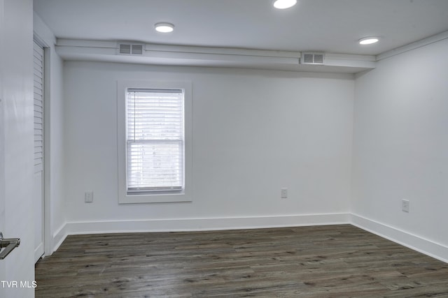 empty room featuring dark wood-type flooring, visible vents, and baseboards