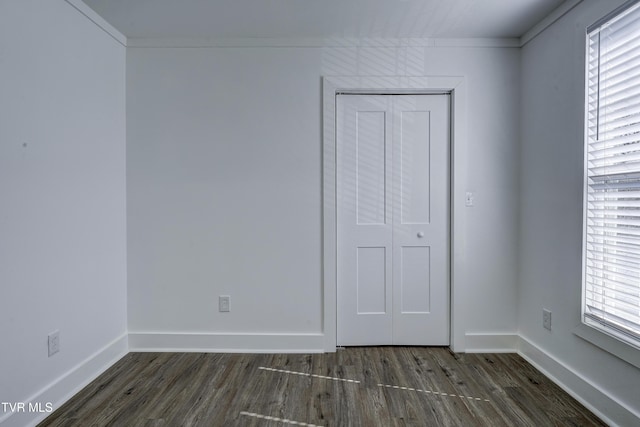 unfurnished bedroom featuring a closet, baseboards, dark wood-type flooring, and ornamental molding