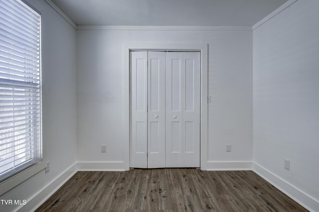 unfurnished bedroom featuring crown molding, a closet, dark wood finished floors, and baseboards