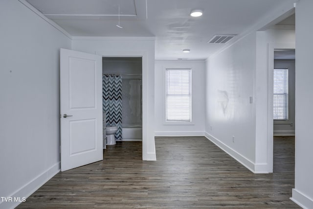 unfurnished bedroom featuring attic access, crown molding, dark wood finished floors, and visible vents