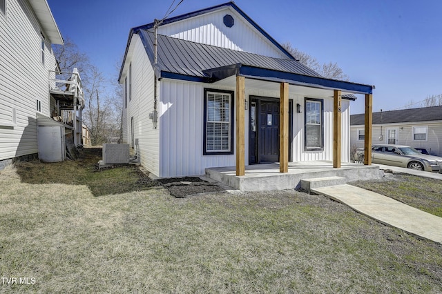 view of front facade featuring central AC unit, metal roof, covered porch, a front lawn, and board and batten siding