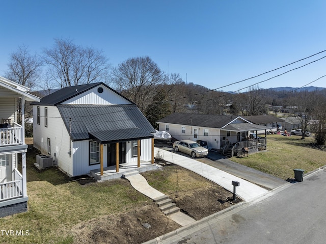 view of front of property featuring covered porch, concrete driveway, a front yard, metal roof, and a residential view