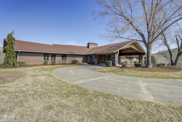 ranch-style home featuring concrete driveway, brick siding, a chimney, and a front lawn