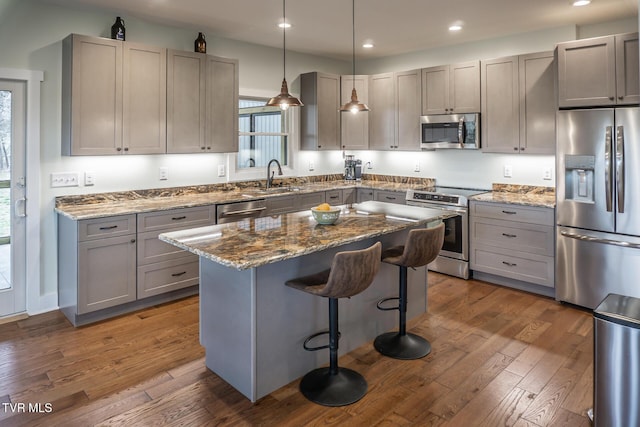 kitchen featuring stone counters, dark wood-style flooring, gray cabinetry, appliances with stainless steel finishes, and a sink