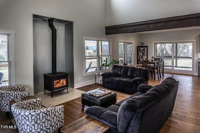 living room with a wood stove, a towering ceiling, baseboards, and wood finished floors