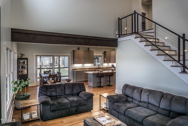 living area with light wood finished floors, stairway, a towering ceiling, and baseboards