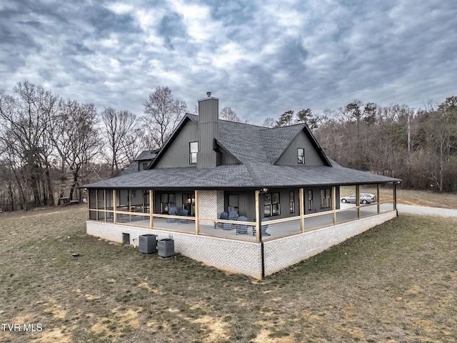 view of side of property with a shingled roof, cooling unit, a sunroom, and a chimney