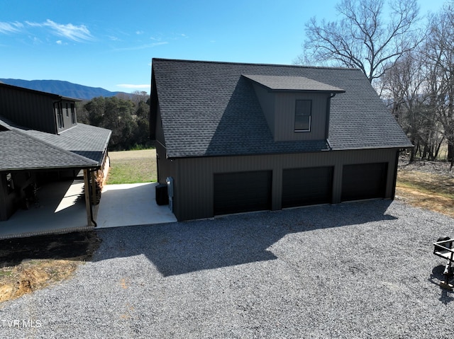 view of side of property with a garage, a shingled roof, and a mountain view