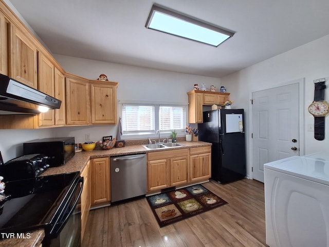 kitchen featuring light wood finished floors, washer / dryer, under cabinet range hood, black appliances, and a sink