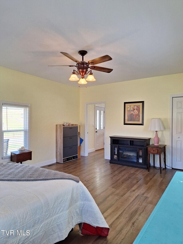 bedroom with a ceiling fan, baseboards, wood finished floors, and a glass covered fireplace