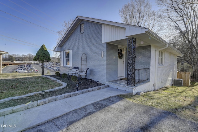 view of front facade featuring brick siding, a front lawn, a porch, and cooling unit