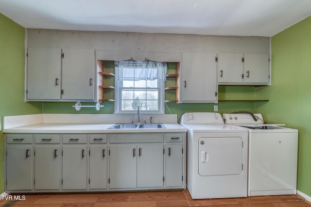 laundry area with light wood finished floors, washer and clothes dryer, a sink, and cabinet space