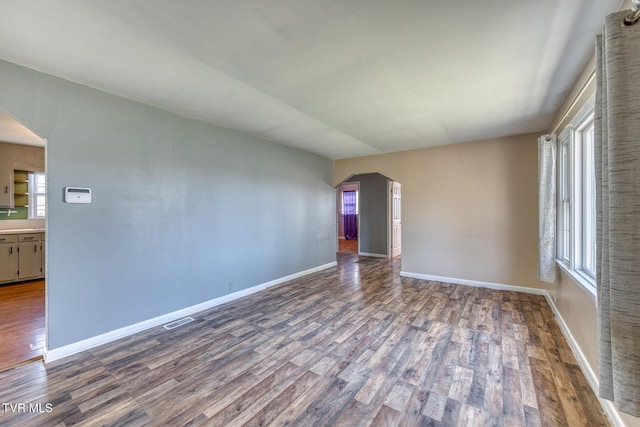 unfurnished room with arched walkways, visible vents, baseboards, and wood finished floors