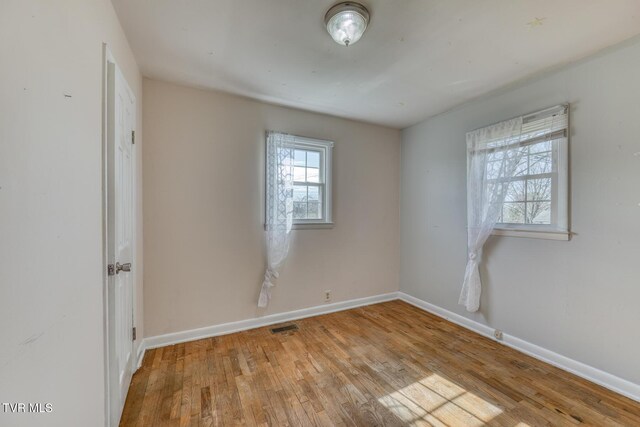 unfurnished room with wood finished floors, visible vents, and baseboards